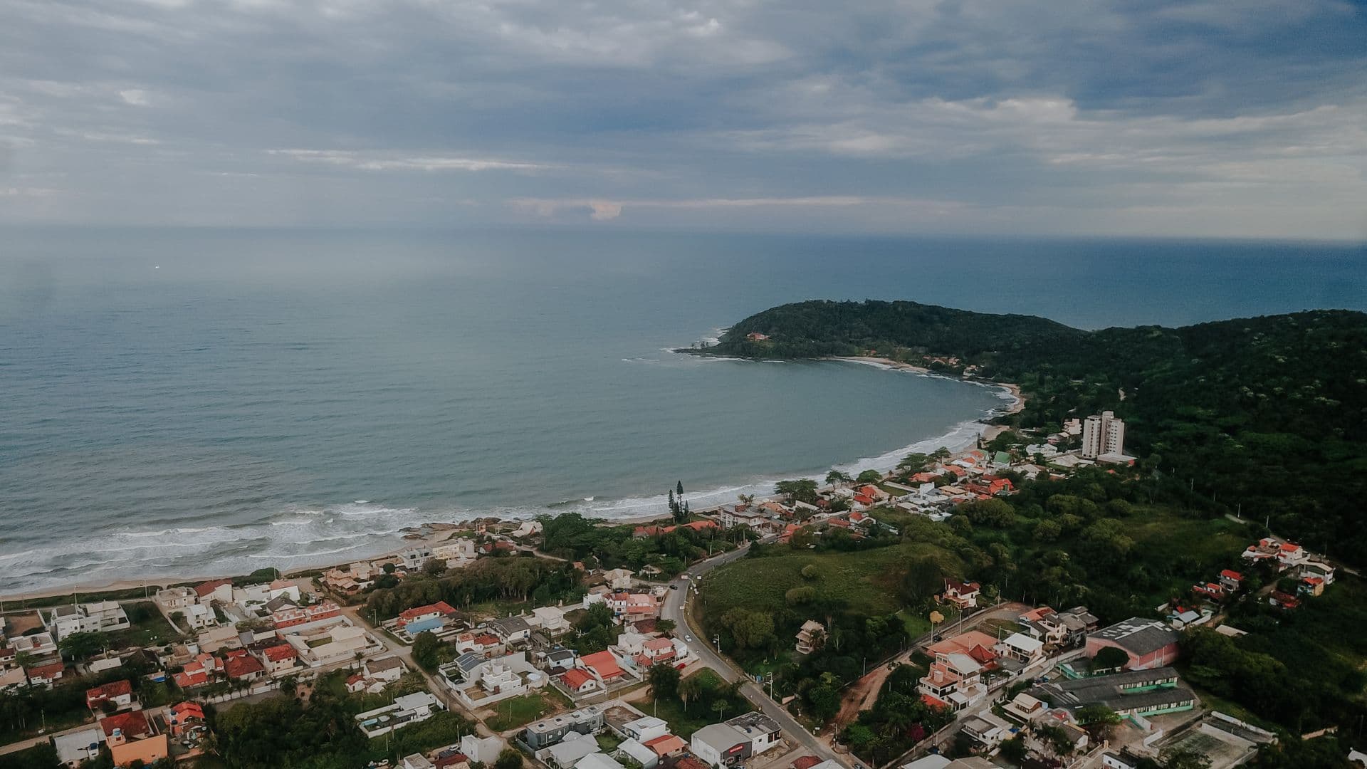 Vista aérea do litoral de Penha com praia, mar, morros e a cidade junto à costa
