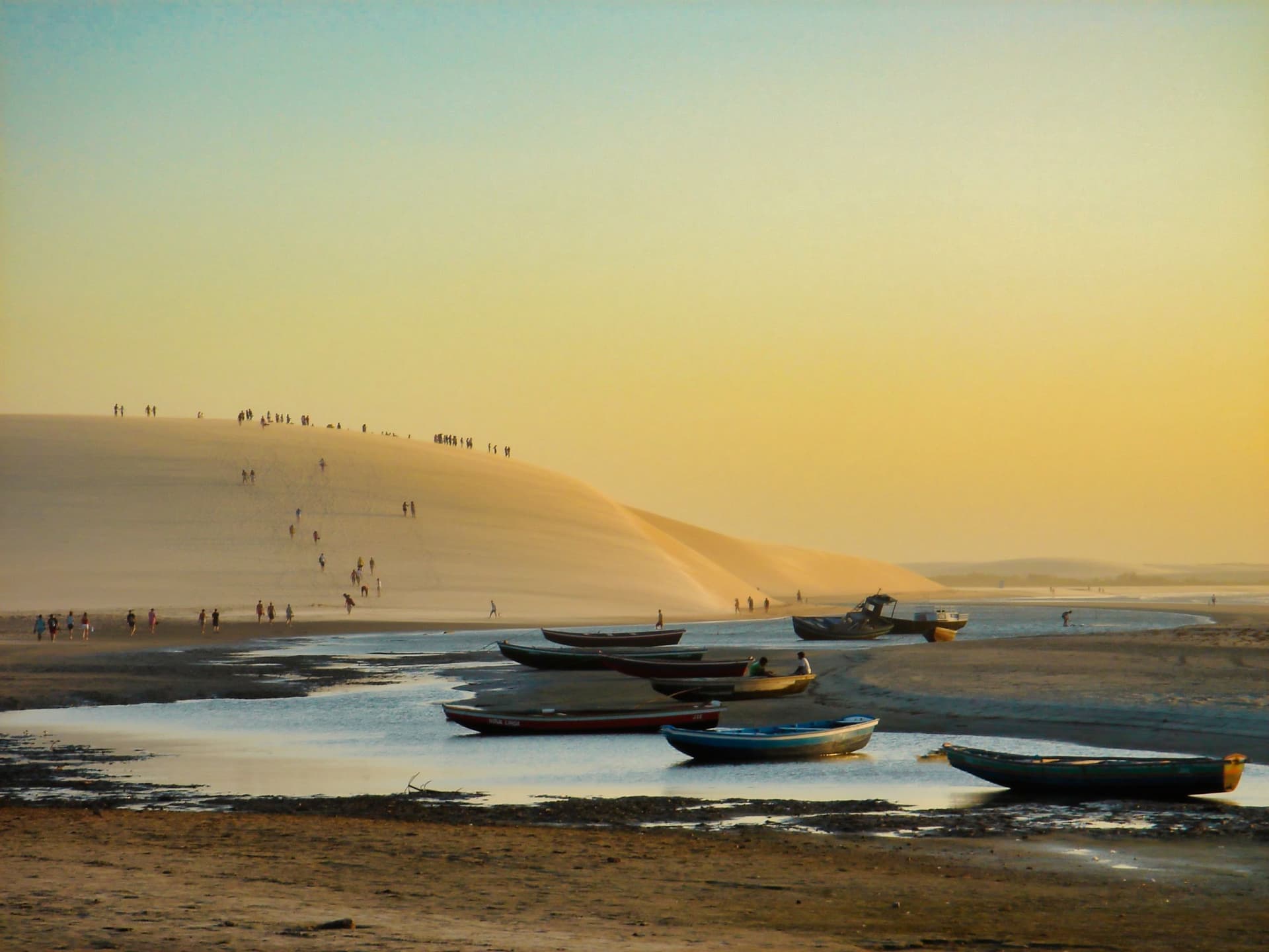 Duna do Pôr do Sol de Jericoacoara ao entardecer, com jangadas na areia e pessoas subindo a duna