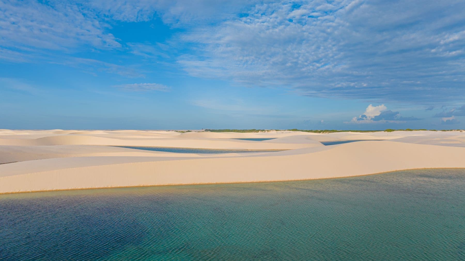 Dunas brancas e lagoas dos Lençóis Maranhenses sob céu azul com nuvens