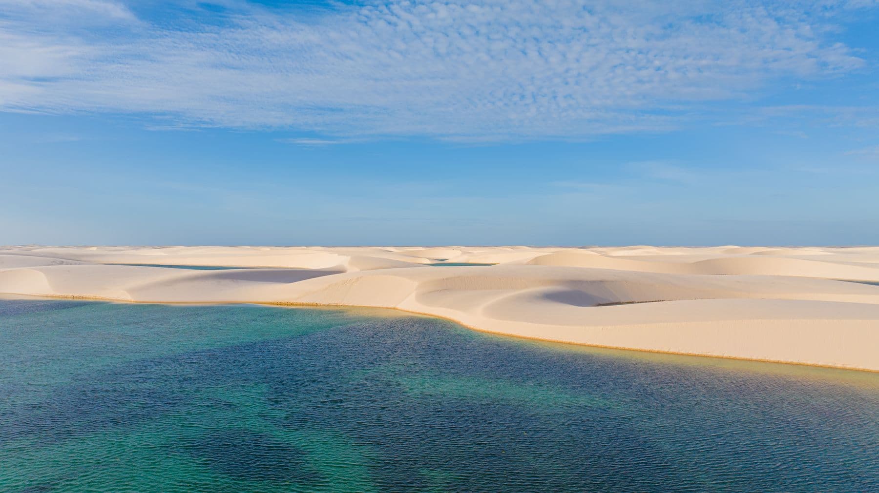 Lagoa de água azul-esverdeada à beira das dunas dos Lençóis Maranhenses
