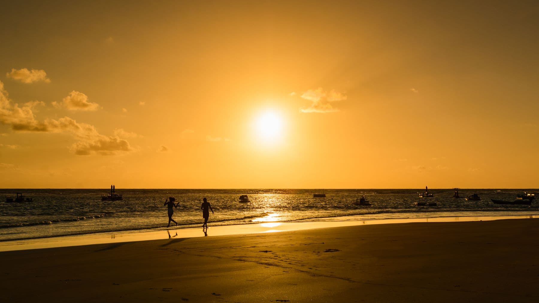 Pôr do sol dourado sobre o mar de Porto de Galinhas, com silhuetas caminhando na areia
