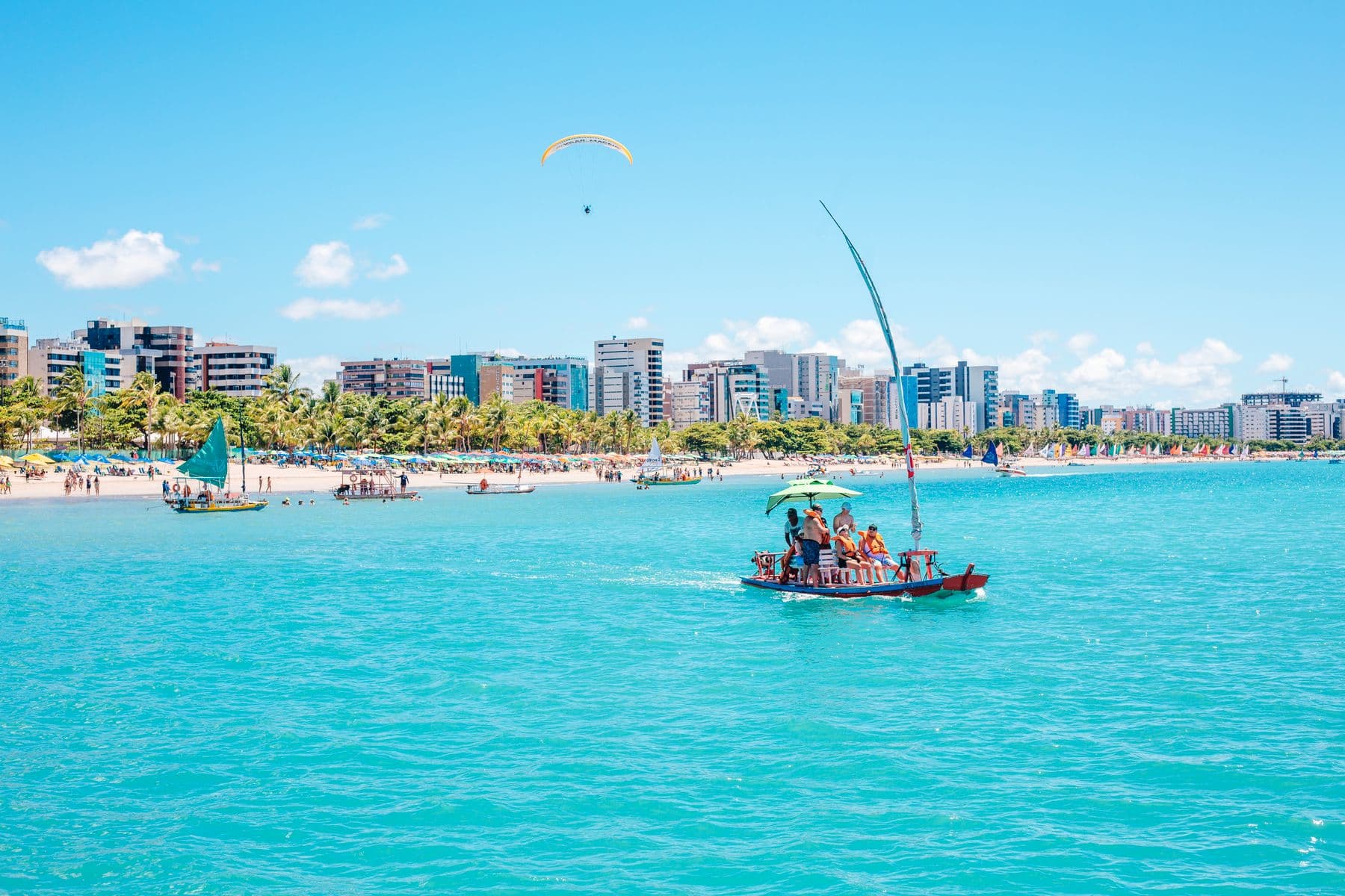Passeio de jangada nas águas turquesa de Maceió, com a orla da cidade ao fundo