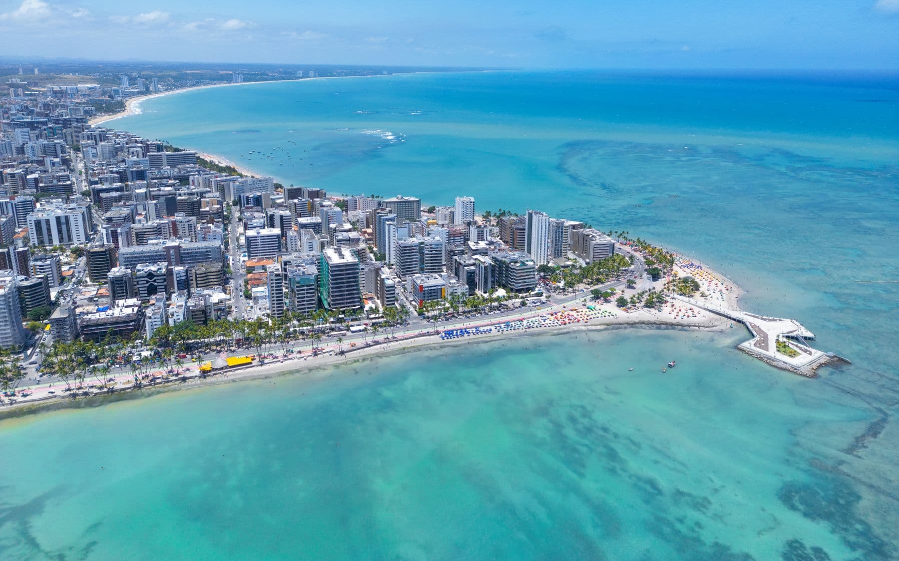 Vista aérea da orla de Maceió, com os recifes desenhando manchas claras no mar