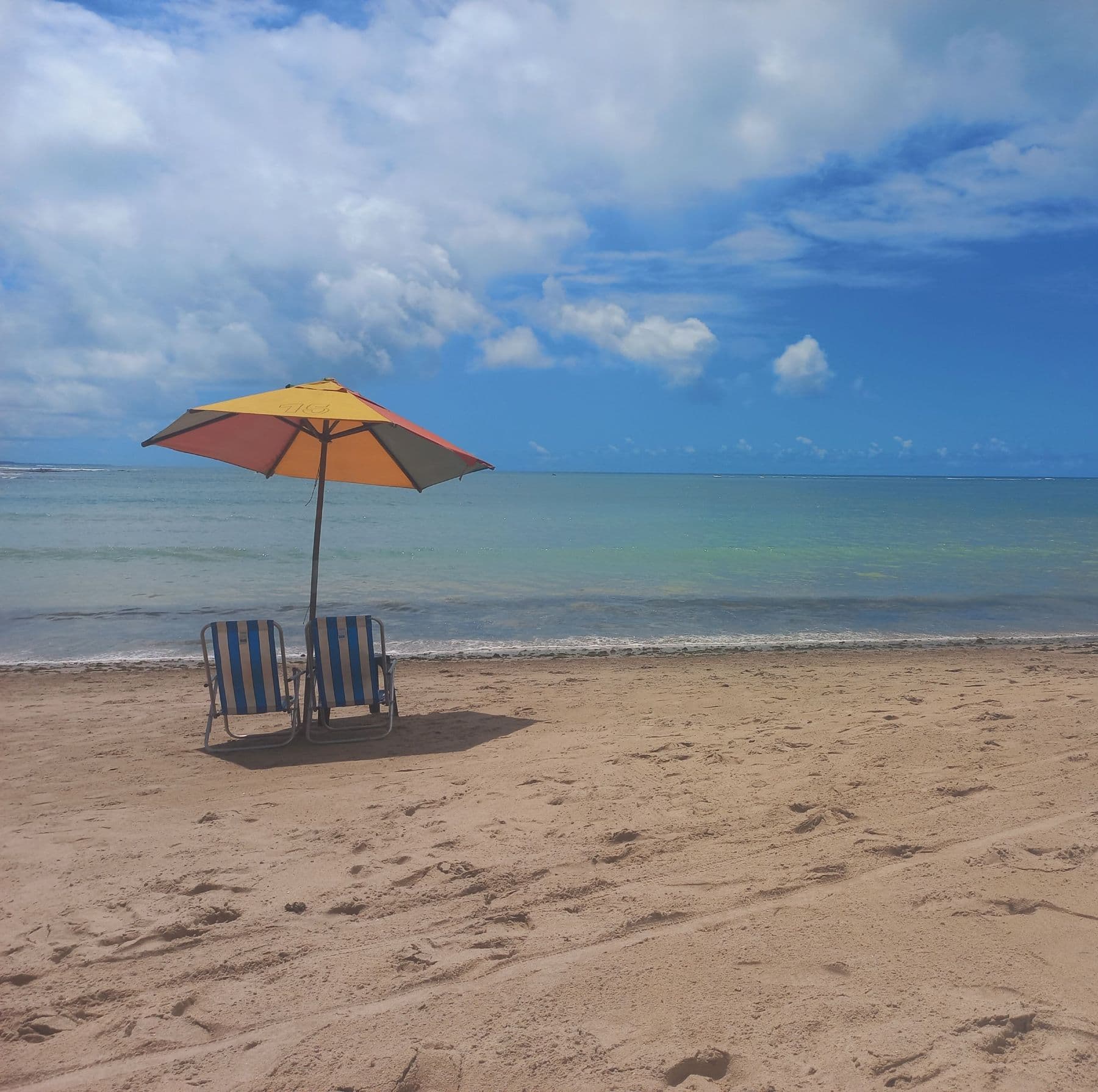 Guarda-sol e duas cadeiras de praia voltadas para o mar, na orla de Maceió