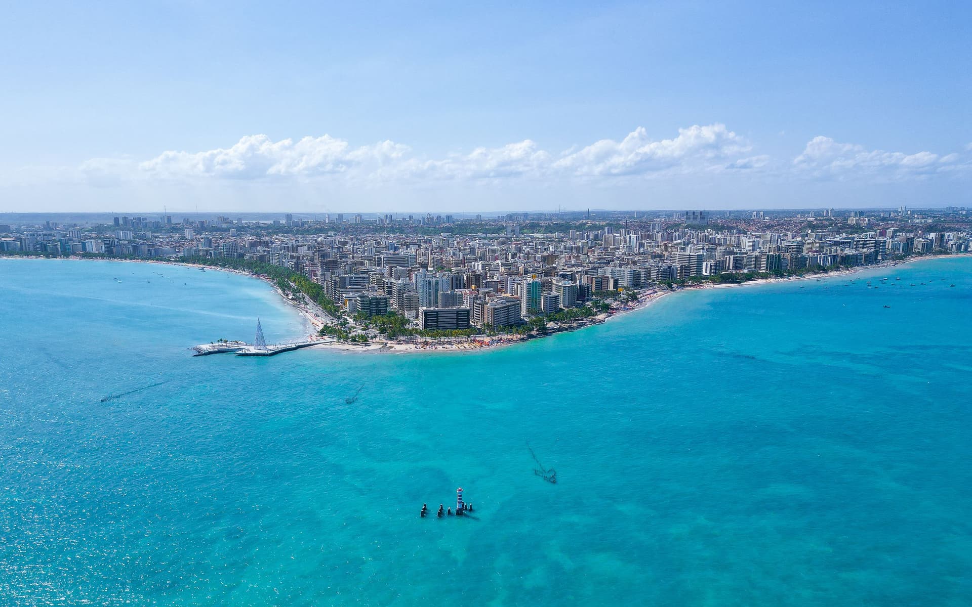 Vista aérea da orla de Maceió, com a faixa de prédios entre a areia clara e o mar turquesa