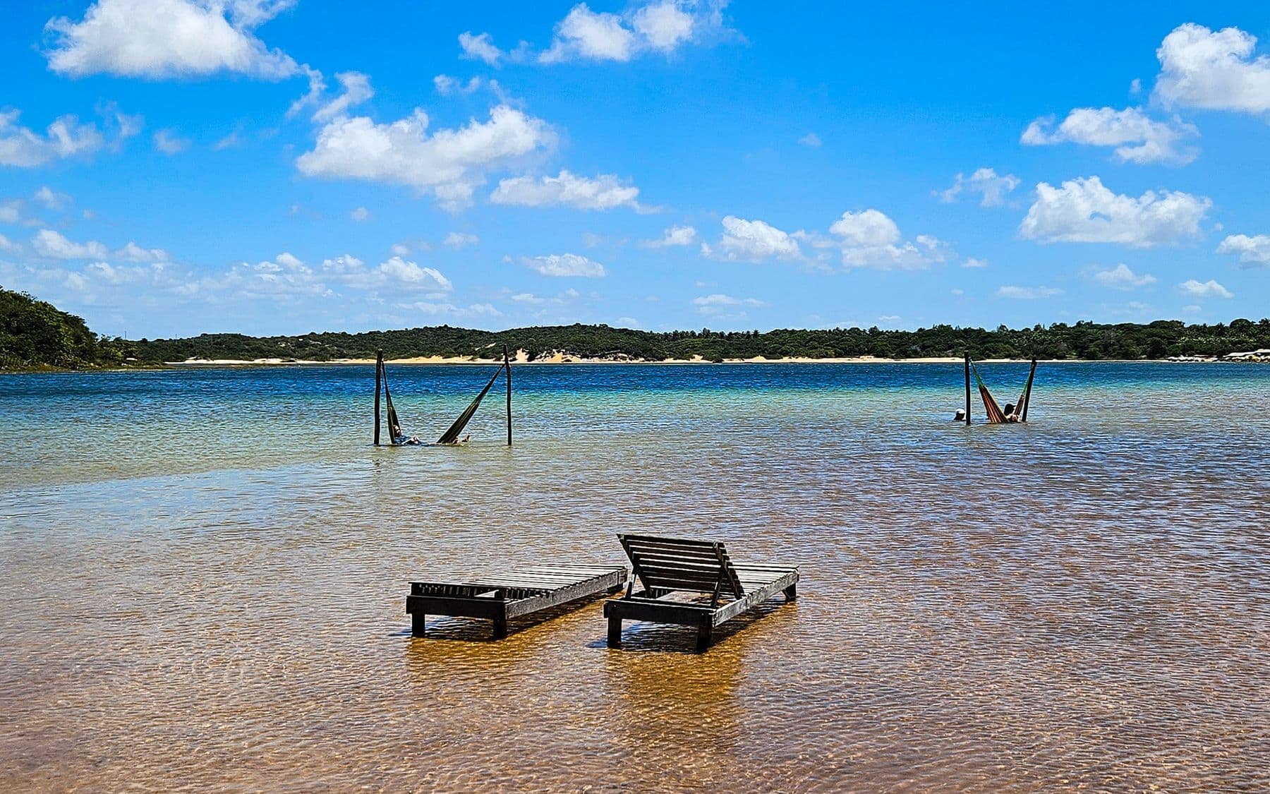Cadeiras e redes dentro da água rasa e transparente de uma lagoa no litoral de Natal